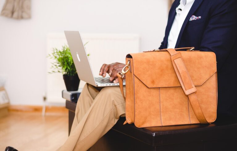 Laptop und lederne Umhängetasche auf einem Tisch mit Zimmerpflanze.