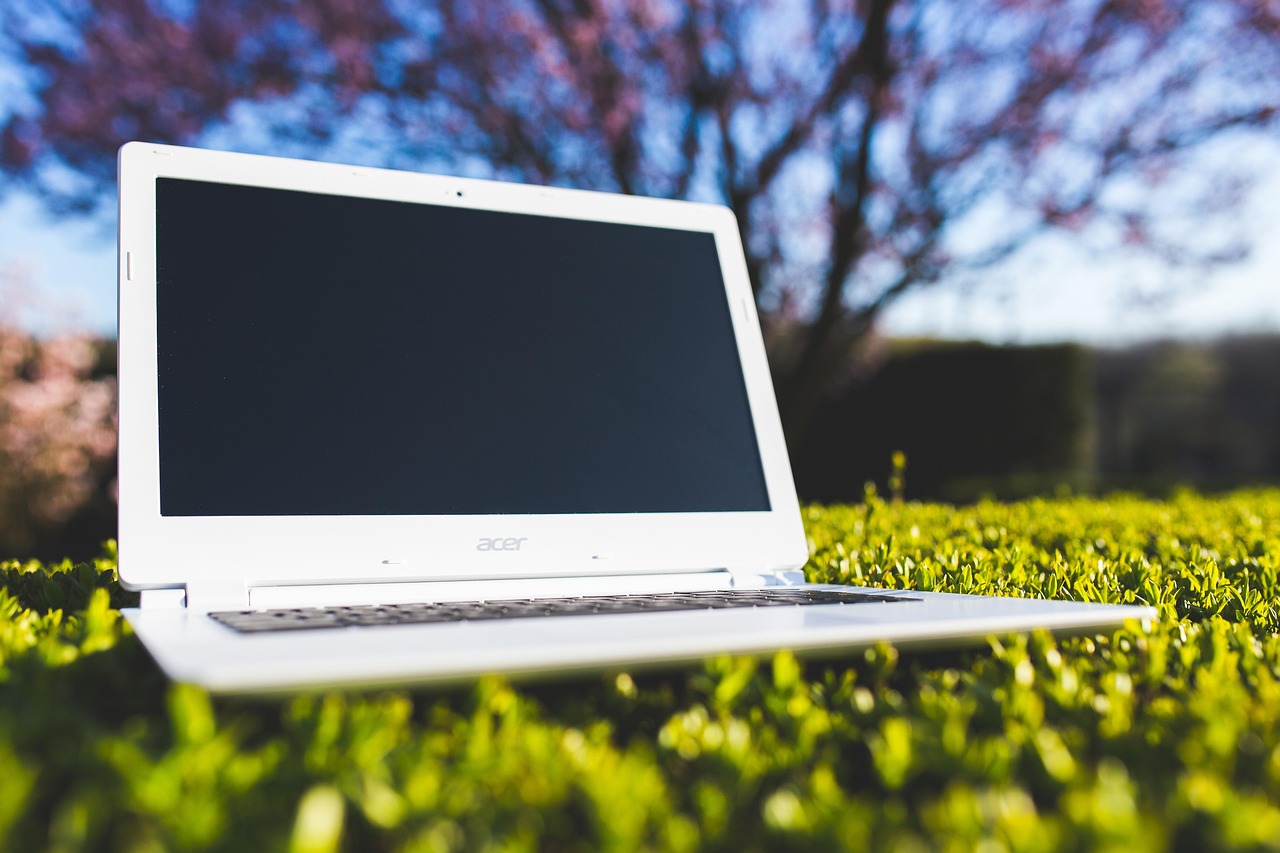 Ein Laptop steht auf einer grünen Wiese bei sonnigem Wetter.