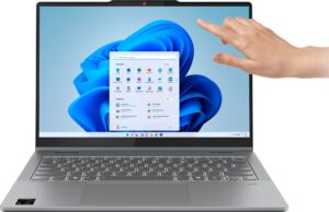 Laptop mit aktivem Windows-Bildschirm und Hand zeigt auf den Touchscreen.